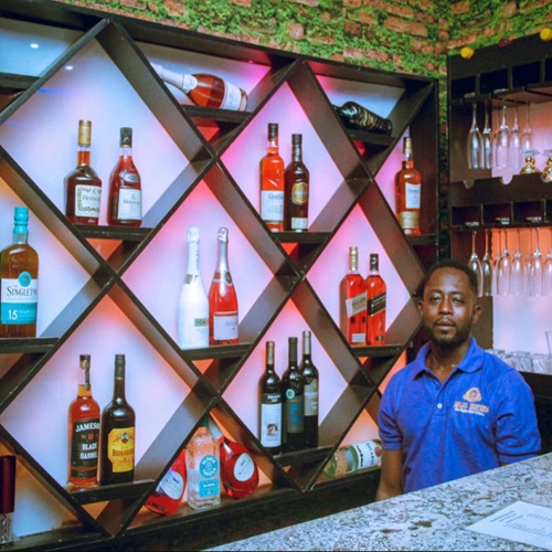 Barman in front of a lit diamond-shaped shelf of spirits and wine
