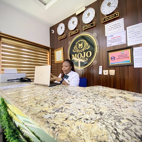 Receptionist at the front desk in front of the gold MOJO Hotels crest