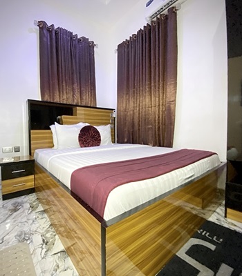 Suite bedroom with a wide bed, burgundy throw and floor-length curtains
